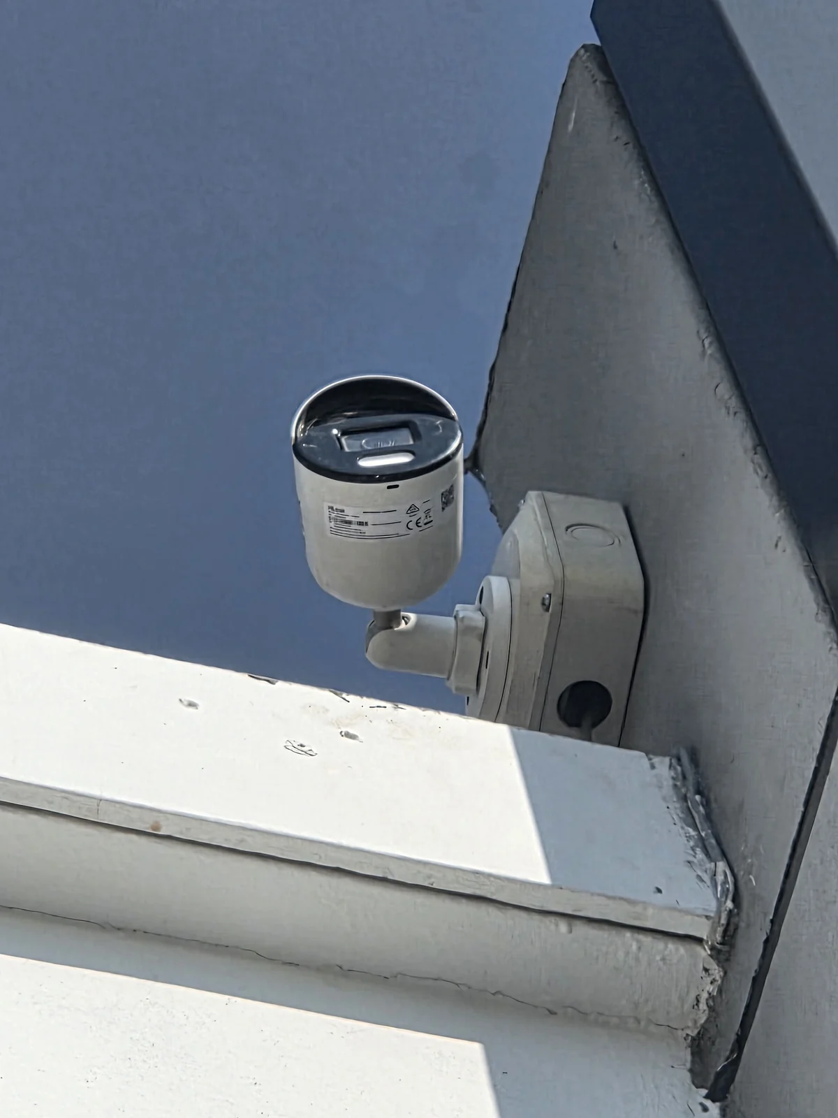An outdoor CCTV camera fixed to a building corner above a roofline, from Anthony Roux’s field-photo collection.